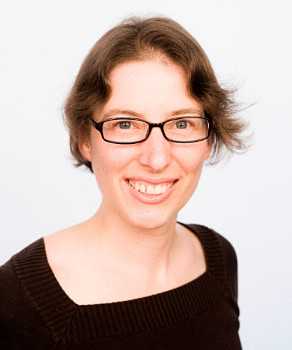 This is a photo portrait of Emilie Combaz, a white middle-aged woman with glasses, short brown hair, and blue eyes. She is smiling.