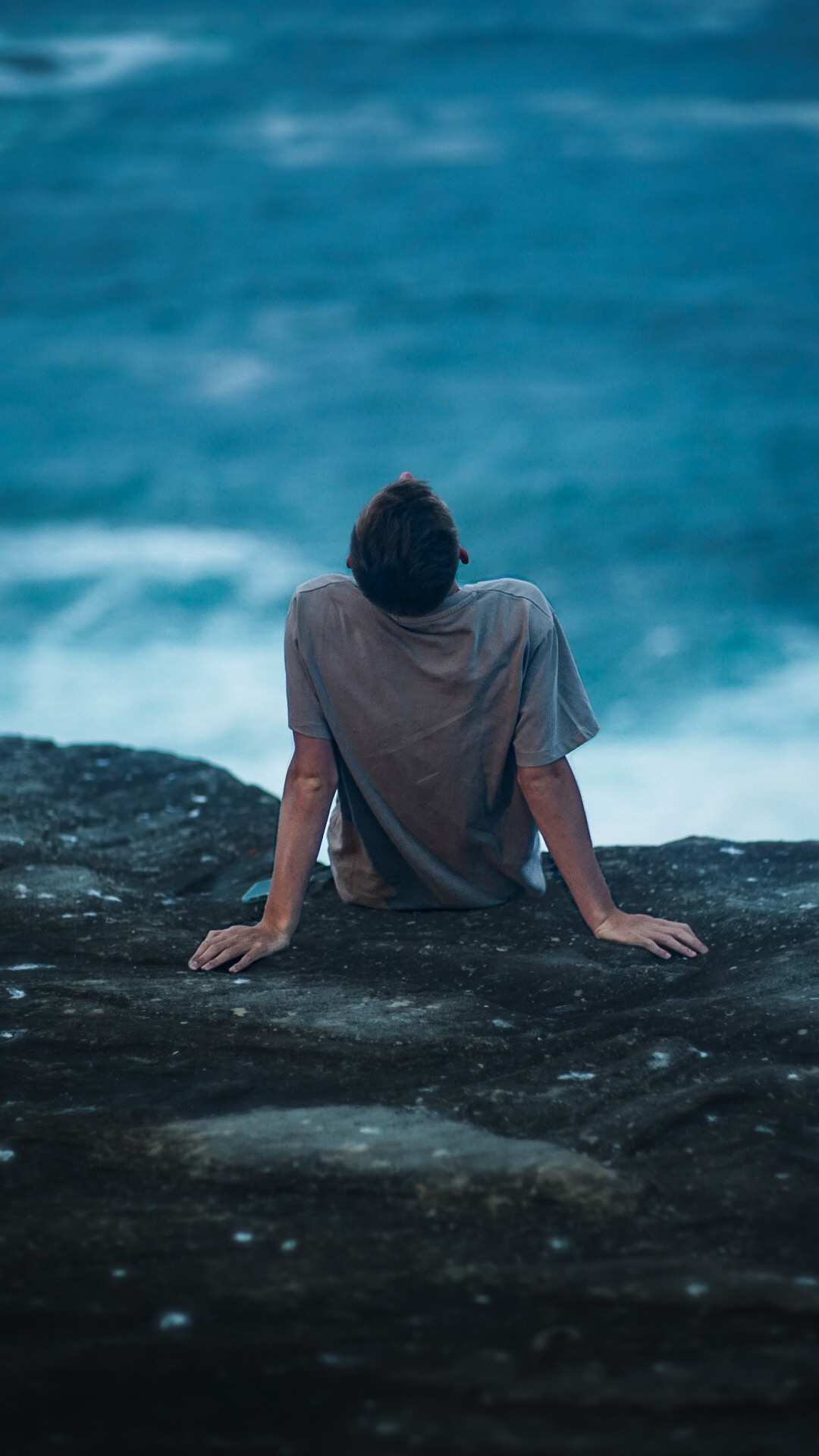 A person sitting on a cliff each leaning back, with the ocean in the background.